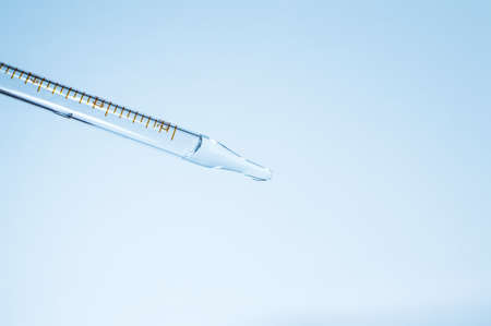 Medical laboratory. Pipette with a clear liquid on a blue background. Laboratory tests. Close-up.