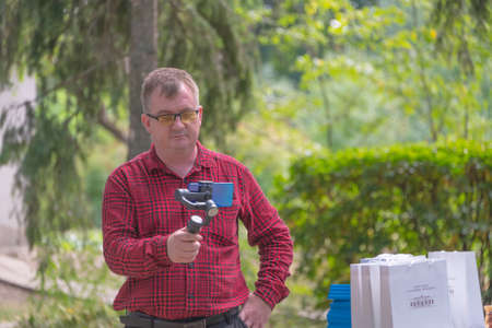 a man in a red shirt and glasses takes pictures of nature on his phone.