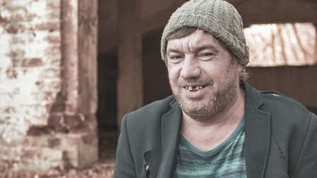 a poor homeless man in a hat and suit smiles looking at the camera in modern society, the concept of...