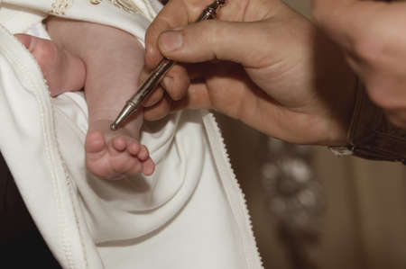 The priest smears the baby's leg with oil at the baptism ceremony in the church. Religion. Close-up.