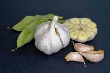 Side view of a whole garlic bulb, half a garlic bulb, garlic cloves and bay leaves on a dark background. Close-up.の写真素材