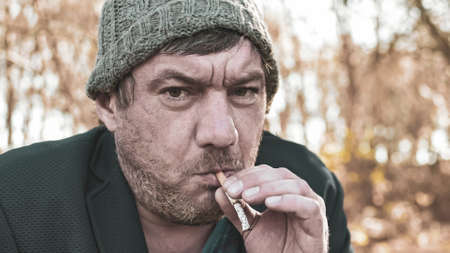 a poor homeless man with dirty hands smokes a cigarette in modern society. Economic recession, unemployment, poverty, hunger, pension, global crisis, the concept of the problem of inequality.の写真素材