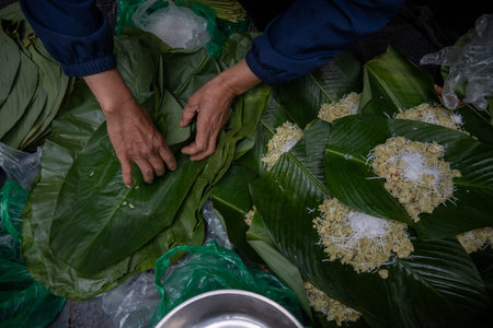 Hands Preparing Traditional Vietnamese Sticky Rice Cakes with Coconut on Banana Leaves, Making Banh It or Banh Chung, Authentic Southeast Asian Culinary Process and Street Foodの写真素材