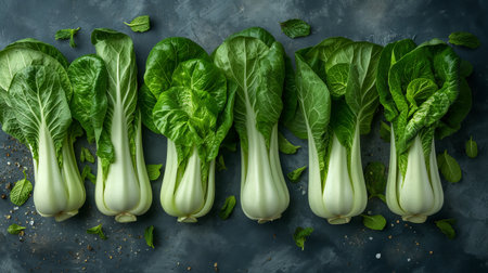 Fresh baby bok choy lines up in a neat row, their vibrant green leaves glistening with tiny water droplets against a dark, moody backdrop.の素材
