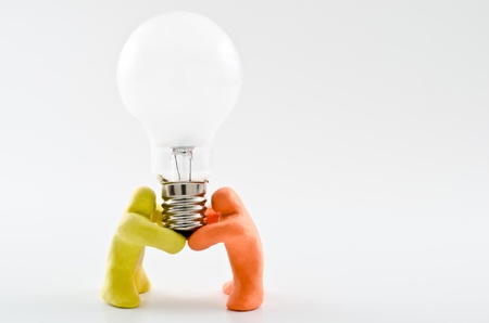 Two dolls supporting light bulb over gray