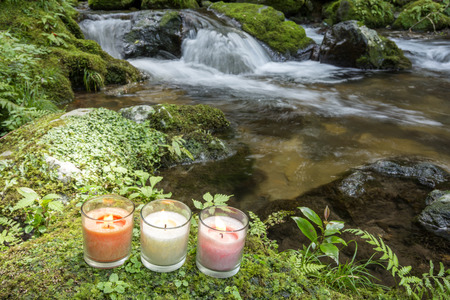 Three glass candles on mossy stone at riversideの写真素材