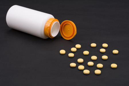 Yellow vitamin pills and sideways bottle on dark backgroundの写真素材