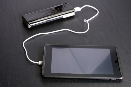 Charging tablet in front of portable rechargeable battery on black deskの写真素材