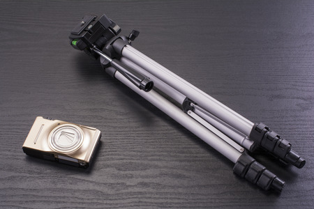 Compact digital camera and small tripod on black deskの写真素材