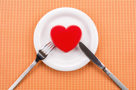Knife and fork attached to vivid red heart on white plate