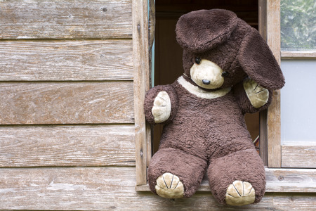 Front view of old stuffed bear on windowsill of wooden buildingの写真素材