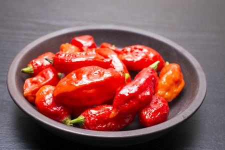 Several red Bhut Jolokia fruit on earthen round plateの写真素材