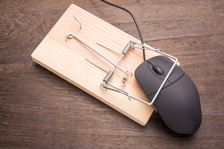 Computer mouse caught by the mousetrap device on wooden tableの写真素材