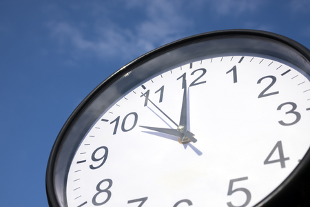 Black frame round wall clock under blue sky