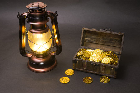 Lighting copper color LED LED lantern and treasure chest with gold coins in front of dark backgroundの写真素材