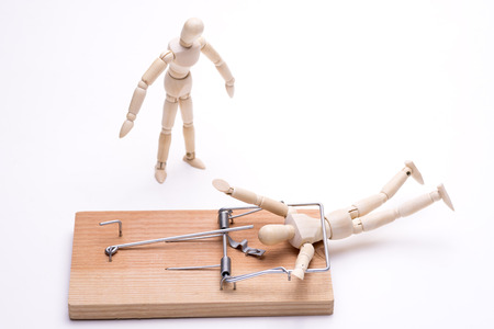Wooden doll caught in a mouse trap and bystander in front of white backgroundの写真素材