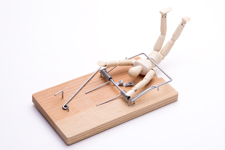 Wooden doll caught in a mouse trap in front of white backgroundの写真素材