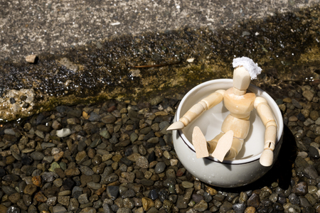 Wooden doll in a pottery tub of spa beside river on gravelsの写真素材