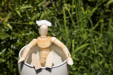 Front facing wooden doll in a pottery tub of spa in front of green grasslandの写真素材