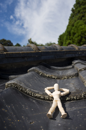 Wooden doll sleeping face up on a asian roof tiles in vertical compositionの写真素材