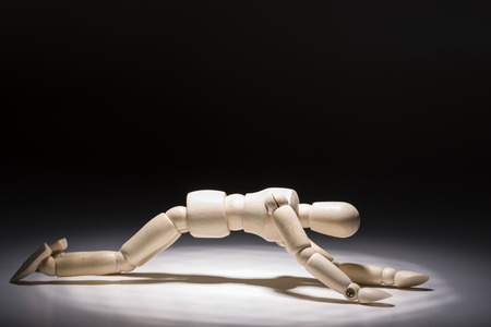 Depressed on all fours wooden doll under a spotlight in front of dark background