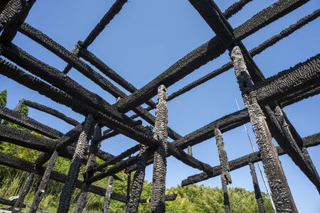 Pillars and beams in a wooden building burnt by fire under blue skyの写真素材