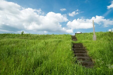 Green grassy place on embankment with stairway under blue skyの写真素材