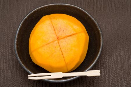 Peeled and cut sweet persimmon fruit on a plateの写真素材
