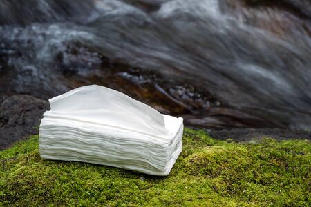 Stacked lot of white tissues on a green moss in front of brook