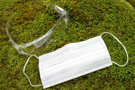 White non-woven face mask and goggles on a green mossの写真素材