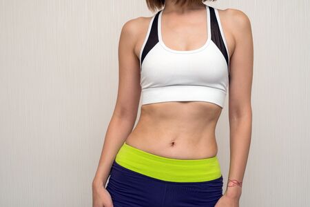 Abdomen of sportswear woman with both hands hanging down in front of light gray wallの写真素材