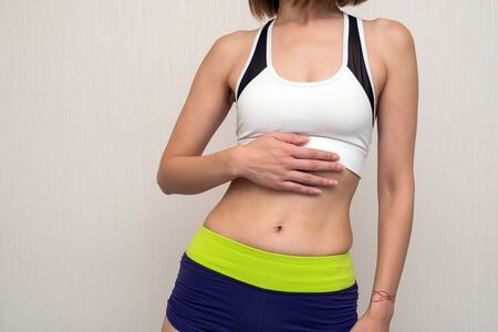 Abdomen of sportswear women her hand on a under the breast in front of light gray wallの写真素材