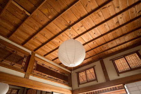 Paper shade pendant lighting hung from wood ceiling in front of two types of transom