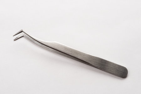 Close up metal bent tip tweezer on the gray paperの写真素材