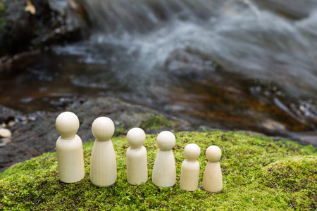 Lined wooden family dolls on a green moss in front of brookの写真素材