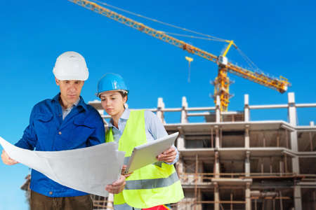 Foreman and engineer with blueprints at construction siteの写真素材