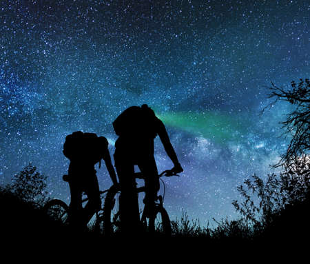 Couple ride bicycles at night under the milky wayの写真素材