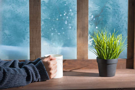 Cozy woman in knitted winter warm woolen sweater on a window sill 
