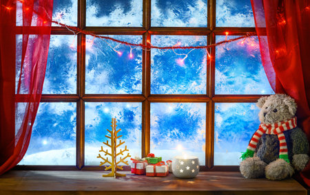 christmas cozy interior background with window sill illuminated with lights and teddy bear toyの写真素材