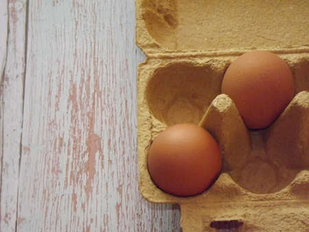 beige chicken eggs in an egg box on a light wooden background. High quality photo