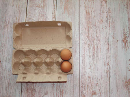 beige chicken eggs in an egg box on a light wooden background. High quality photoの写真素材