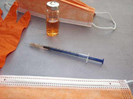 on a gray background, a vaccine, a syringe, orange medical masks and gloves. High quality photo