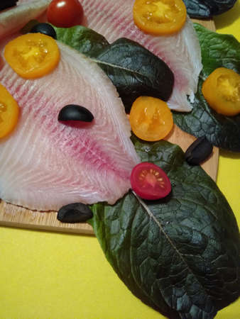 the process of cooking tilapia fish fillet with tomatoes, olives and lettuce leaves. High quality photoの写真素材