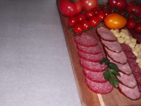 slicing smoked sausage of four varieties with cheese and red and yellow tomatoes and cherry...