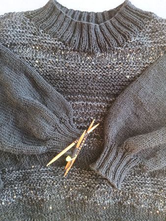 The process of knitting a jumper made of black and gray wool with sequins. High quality photo