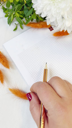 Creative Workspace with Hand Holding Pencil and White Chrysanthemumsの写真素材