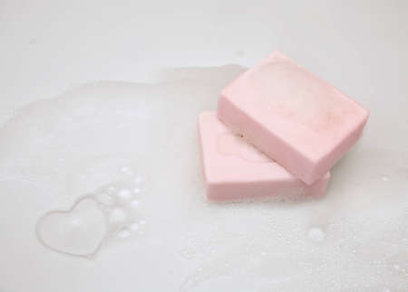 Two pieces of pink scented soap and the heart in a cloud of foamの写真素材