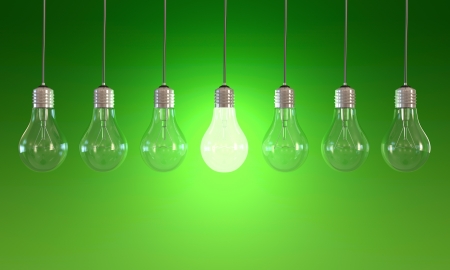 Seven light bulbs with lit one on green backgroundの写真素材