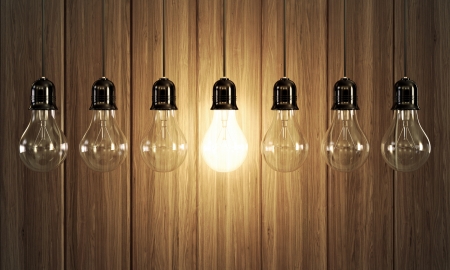 Seven light bulbs with glowing one on wooden background の写真素材