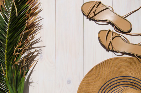 Tropical palm leaf, sun hat and sandals on white wooden background with copy space. Concept for vacation or summer.の写真素材